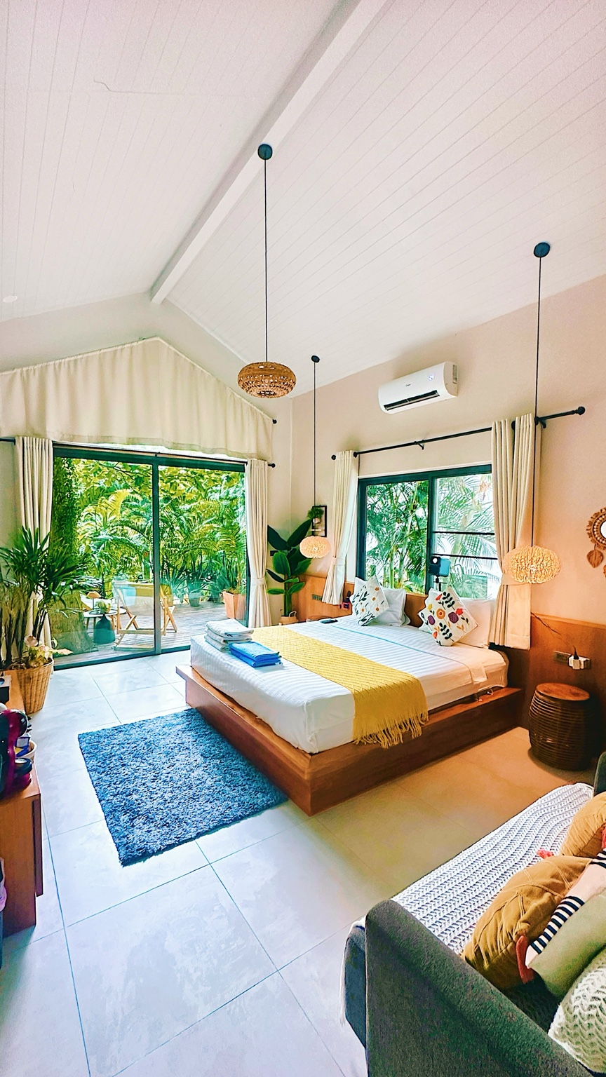 Salad Beach Guest House: wooden bed beneath a high ceiling, with large windows looking onto tropical greenery